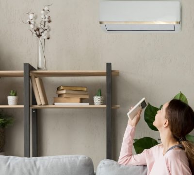 Happy woman rests on couch in modern cozy living room looks up on wall holds cooler system remote controller air conditioner user enjoy fresh air in hot summer day, set comfortable temperature indoors