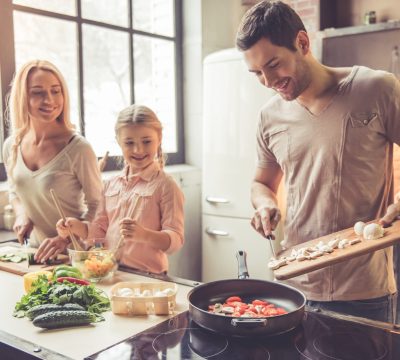 Cute little girl and her beautiful parents are  smiling while cooking in kitchen at home