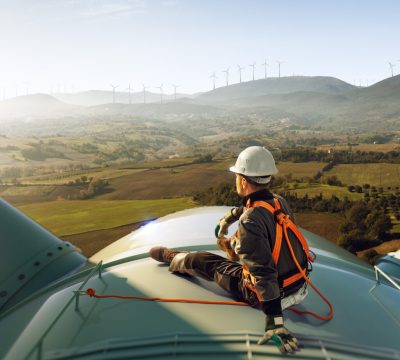 Happy engineer feel success after good work. He standing a top of windmill and looking beautiful sunset landscape